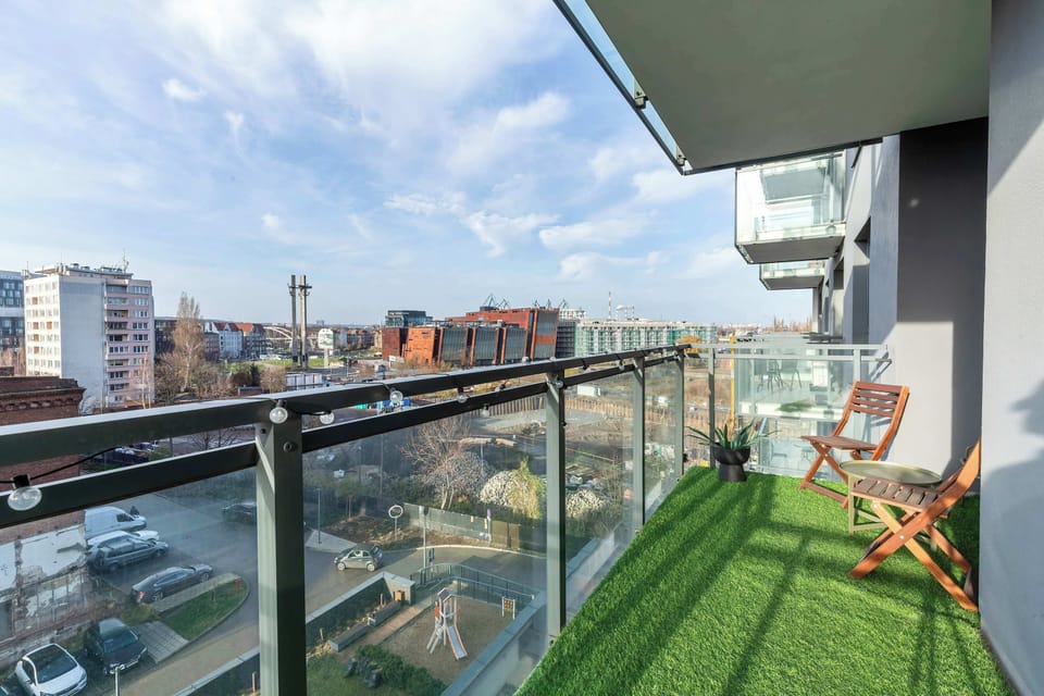 A balcony with outdoor seating and artificial green grass, providing a relaxing space to enjoy the cityscape.