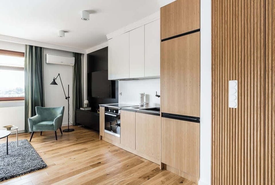 A modern kitchen with a black countertop, open to the living room. The space is stylishly designed with wooden accents and sleek black finishes.