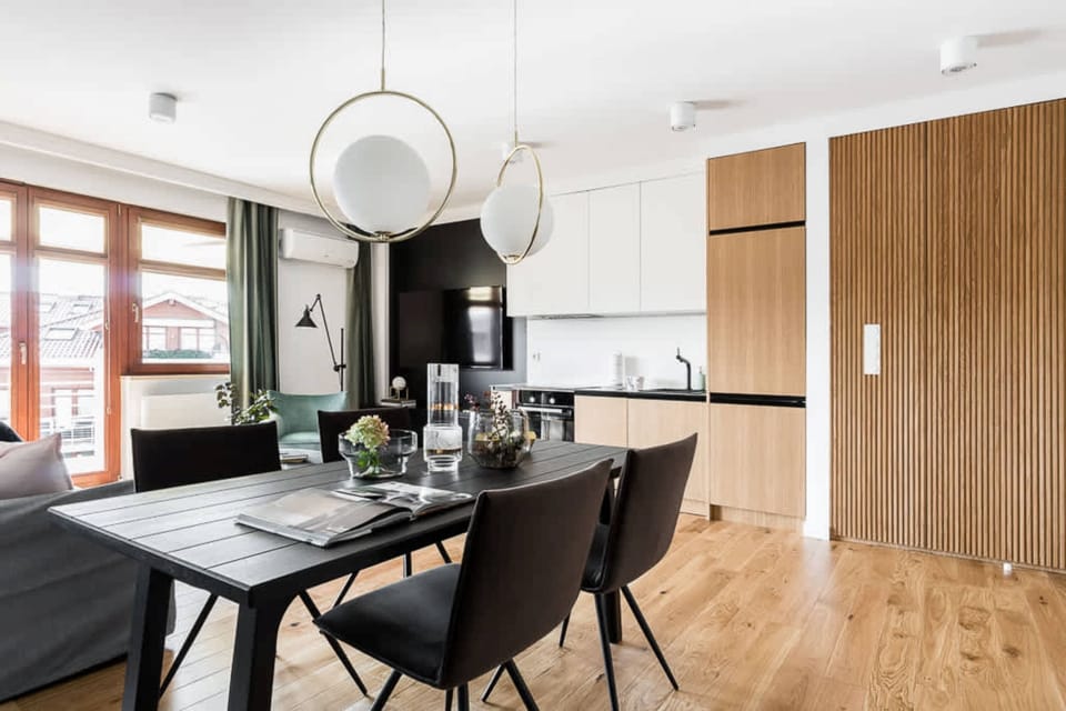 This dining area features a round black dining table with modern, minimalistic chairs. The large window behind offers a view, and a simple, elegant light fixture hangs above.