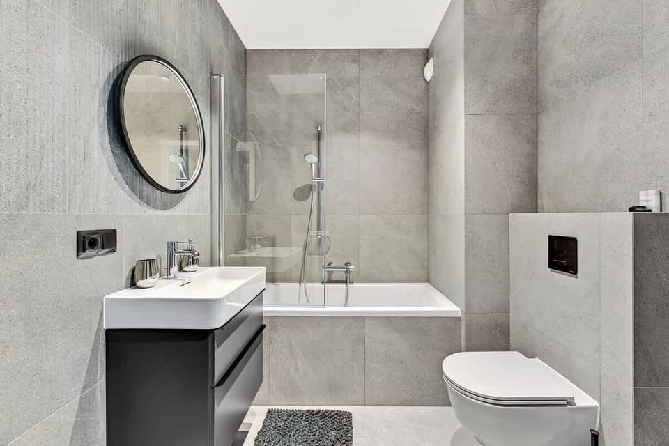 The minimalist-style bathroom has a large bathtub with shower function, toilet, mirror and sink. 