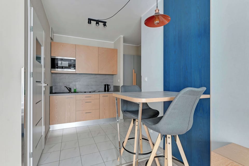 Dining area with a small round table and two chairs. The table is set against a deep blue accent wall, and a modern orange hanging light fixture adds a stylish touch to the space.