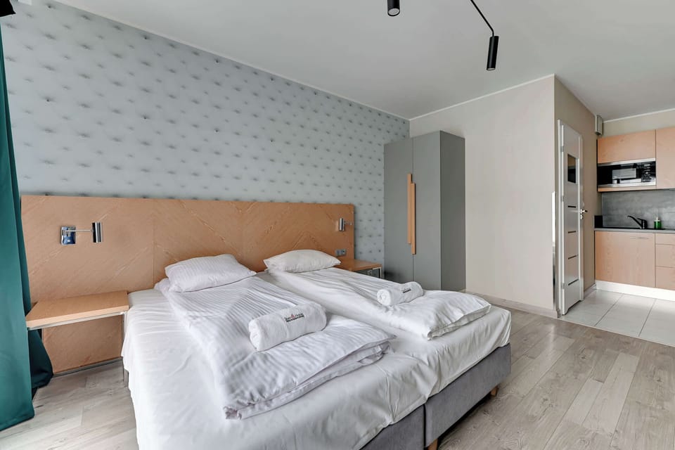 A wide-angle view of the studio apartment, including the bed, kitchenette, and a dining area. The room feels cohesive, with soft, neutral tones and a clean design.