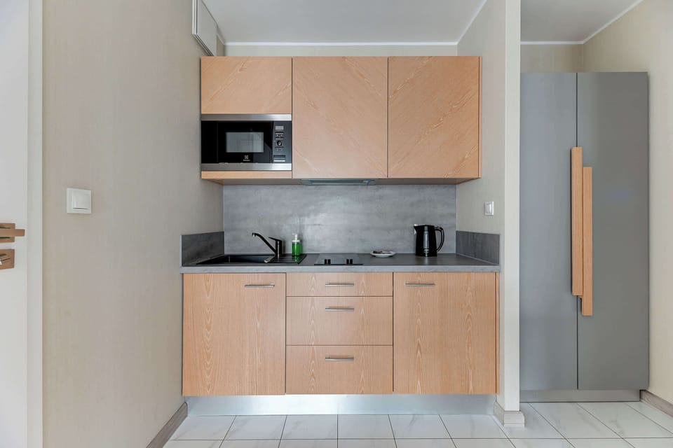 Kitchenette with light wooden cabinets, a microwave, and a minimalist countertop. The functional space is designed to blend seamlessly with the rest of the apartment's modern aesthetic.