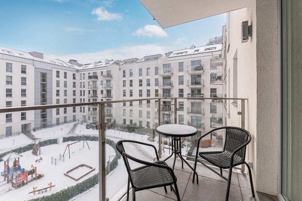 Balcony with a small table and two chairs. It offers a view of an urban courtyard surrounded by white buildings with many windows.