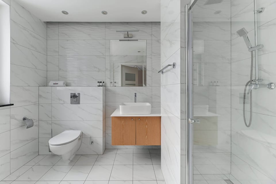 Bathroom with a sleek, modern design. It includes a walk-in glass shower, a floating vanity, and a toilet, all in light marble tones for a luxurious feel.