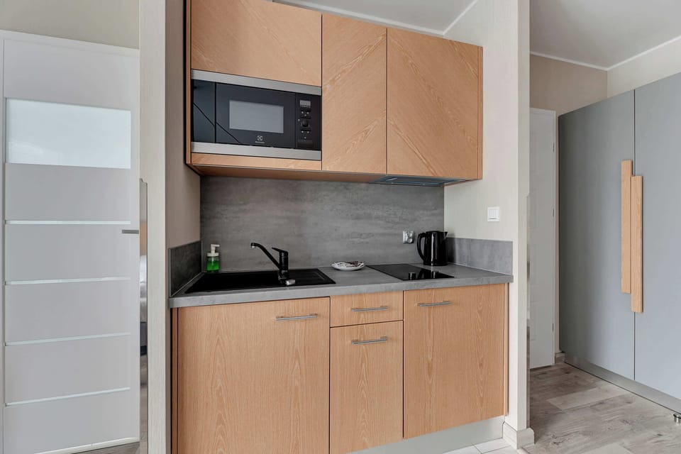 Compact kitchenette with light wood cabinetry and a microwave. The design is minimalistic and efficient, perfect for small-space living.