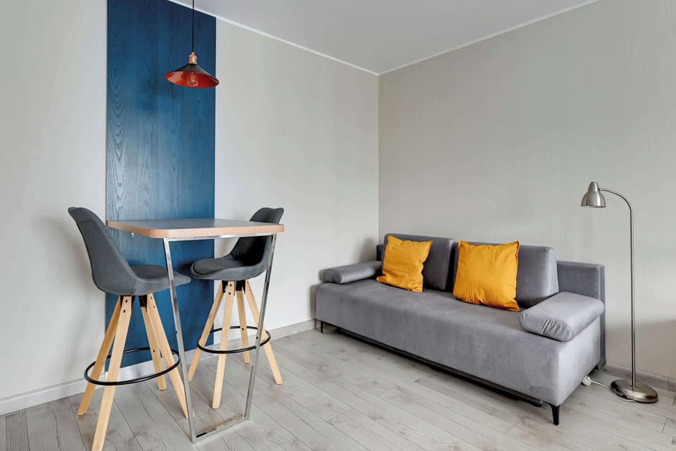 A small seating area with a cozy gray sofa and two mustard-colored cushions. Behind the sofa, there is a deep blue accent wall, adding contrast to the room's light tones.