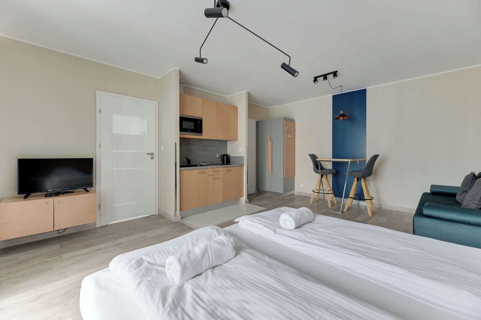 Close-up of the studio, showing the neatly made bed with a wall-mounted TV opposite it. The room is bright and inviting, with soft natural light filtering through the windows.