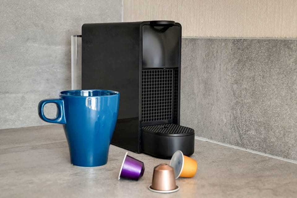 A close-up view of the kitchen highlights its efficient layout, featuring a kettle, cups, and a coffee machine. The gray backsplash complements the wooden cabinetry.