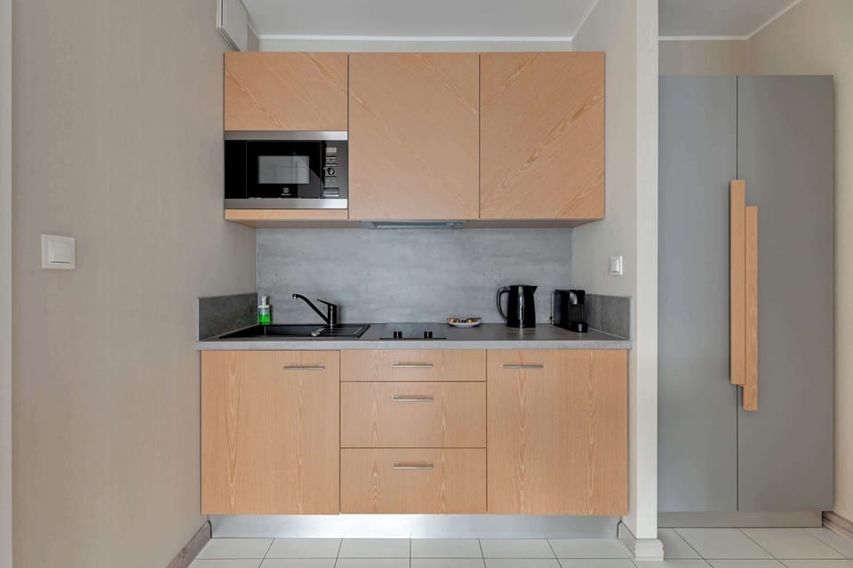 Kitchenette with light wooden cabinets, a microwave, and a minimalist countertop. The functional space is designed to blend seamlessly with the rest of the apartment's modern aesthetic.