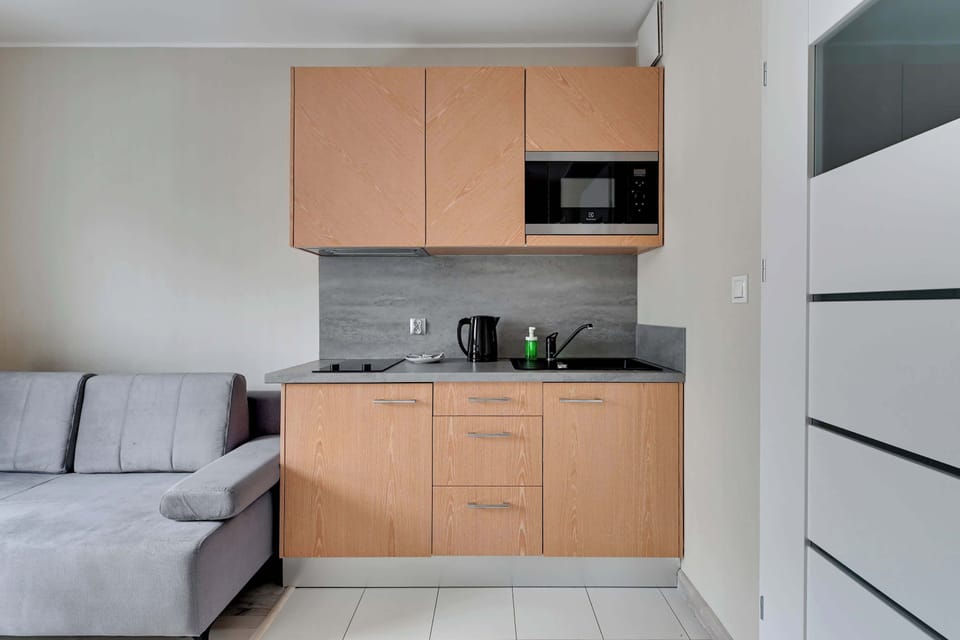 Another angle of the kitchenette showcases its integration with the living area, with light wood cabinetry and a sleek gray backsplash. The space is both functional and visually appealing.