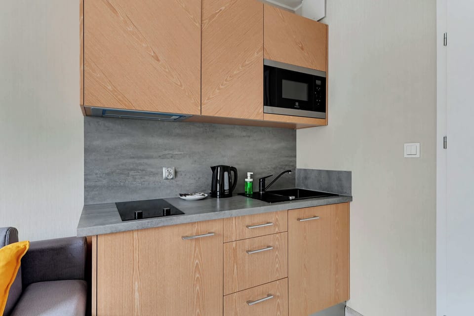 The compact kitchen area has wooden cabinets, a microwave, and essential appliances like a kettle. The design is efficient and matches the contemporary aesthetic of the apartment.