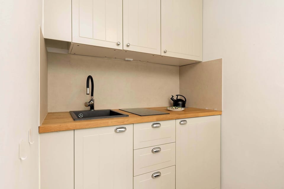 A minimalist kitchenette with sleek white cabinetry, wooden countertop, black faucet, and compact appliances.