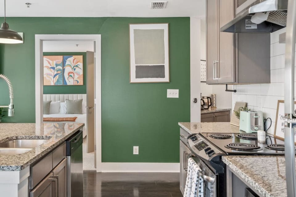 Granite-and-stainless kitchen with green accent wall and bedroom beyond.