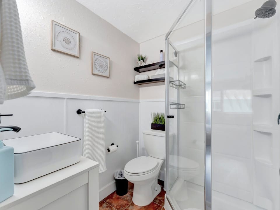 Step into your private bathroom, where a sparkling walk-in shower and crisp white towels await. The thoughtful touches—floating shelves, fresh greenery, and peaceful artwork—create a serene retreat for your morning routine.