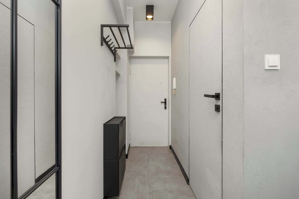 A modern hallway with a white door, a black coat rack, and a mirrored wardrobe that enlarges the space.