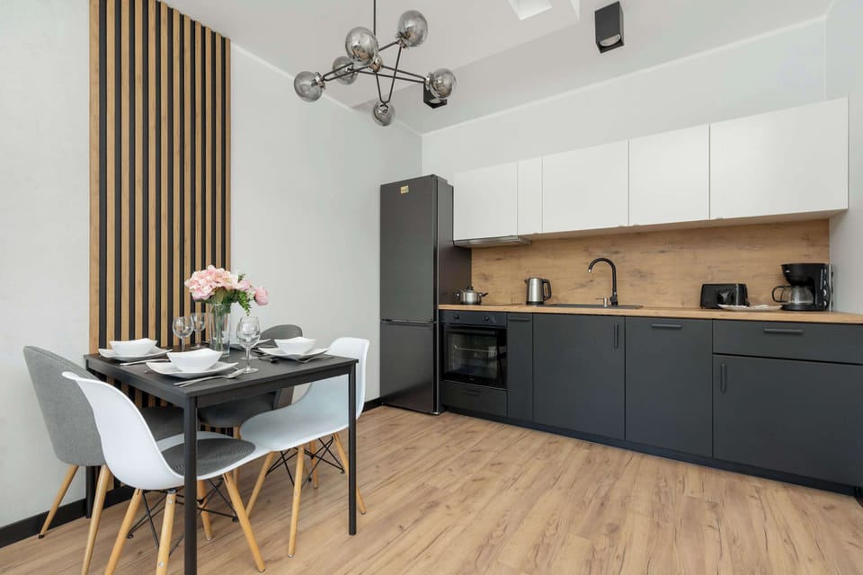 A modern kitchen with sleek white cabinets and a wooden dining table. A unique chandelier adds a touch of elegance.