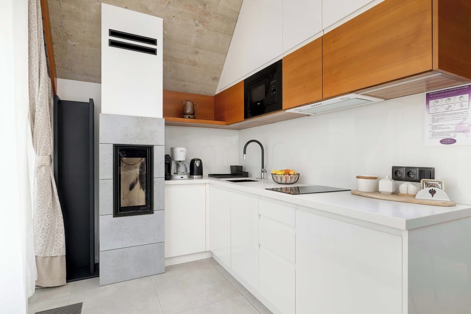 A sleek white kitchen area with built-in appliances, contrasting wooden cabinetry, and a white stove hood.