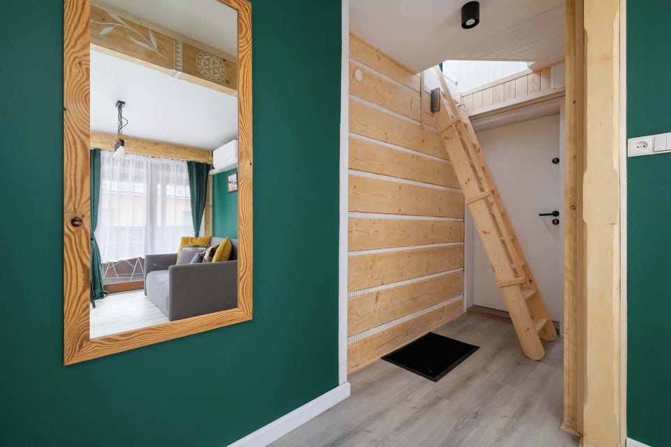 A wooden staircase leads to the bedroom area. A large mirror in a wooden frame hangs on the wall in the hallway.