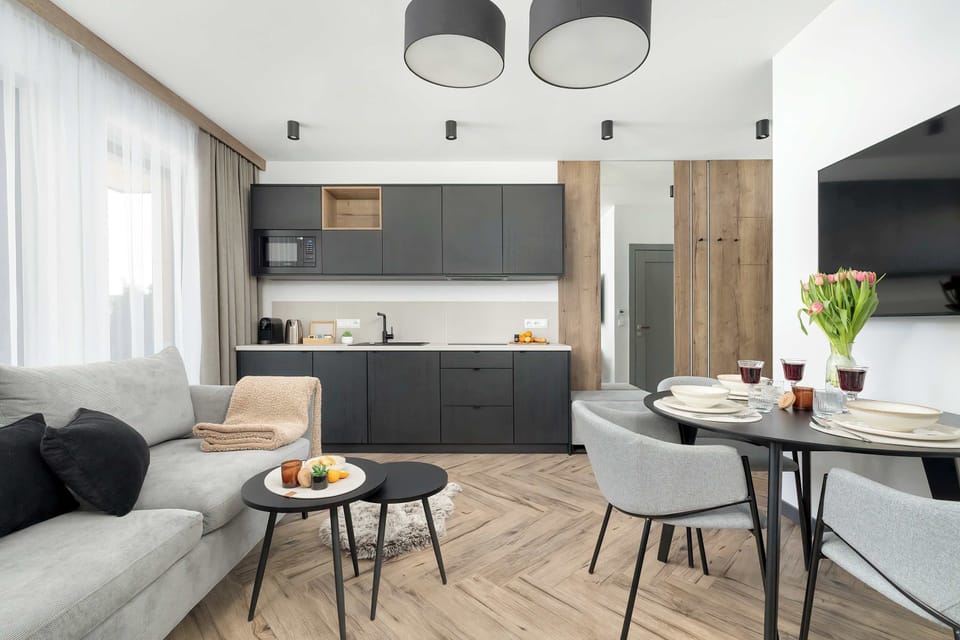 A living room setup with a small dining table and comfortable seating near large windows.
