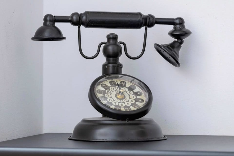 A close-up of a black vintage telephone with an ornate design, placed on a white surface. The intricate details add a classic touch.