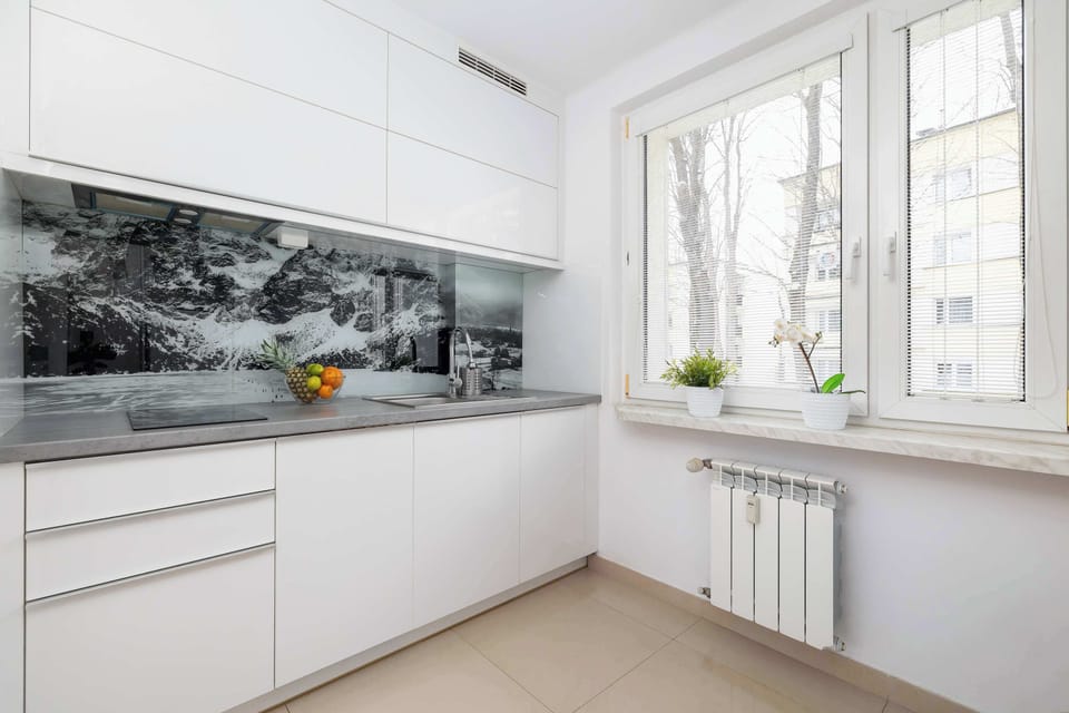 A sleek, modern kitchen with white cabinets and a marble-patterned backsplash. A small breakfast bar with two stools offers additional seating.