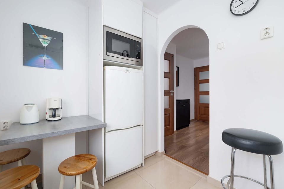 A hallway leading to the kitchen, featuring an arched doorway and a black-and-white color scheme. A small countertop with storage is placed against the wall.