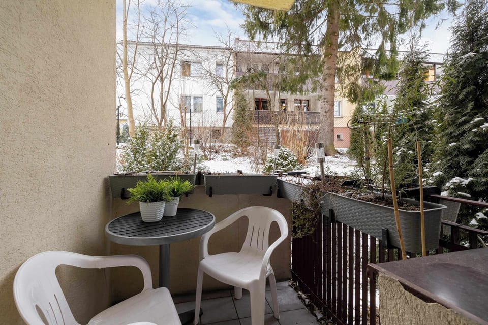A small balcony with a round table and two chairs, surrounded by lush greenery. The peaceful setting is perfect for morning coffee.
