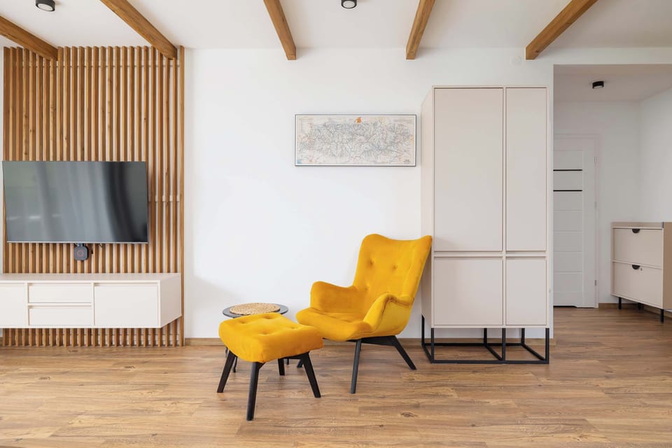 A second view of the living room showing the wooden ceiling beams, open-plan layout, and bright decor.