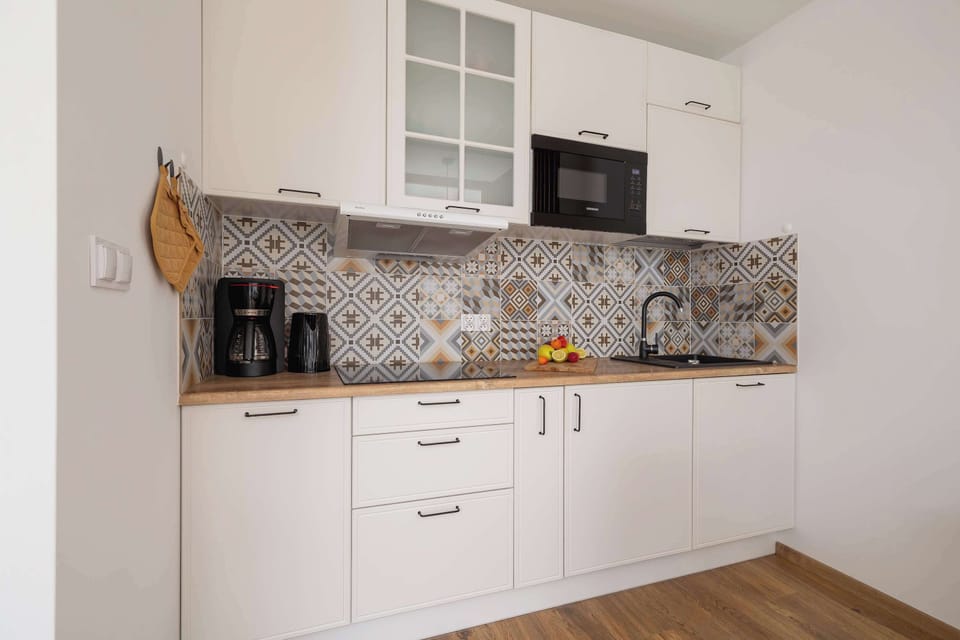 A stylish kitchen with patterned backsplash tiles, white cabinetry, and wood countertops.


