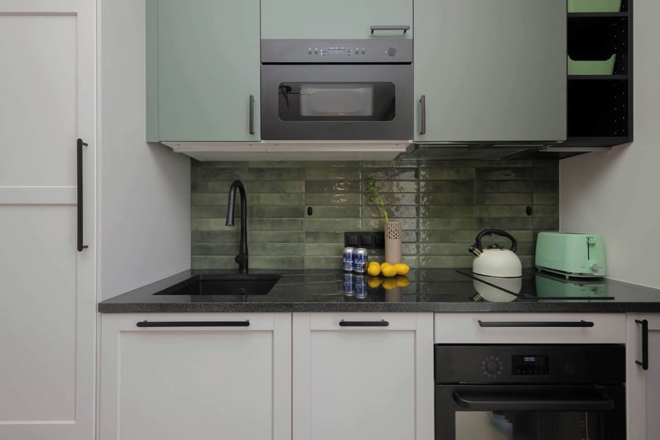 A compact, stylish kitchen with green-tiled backsplash and built-in appliances.