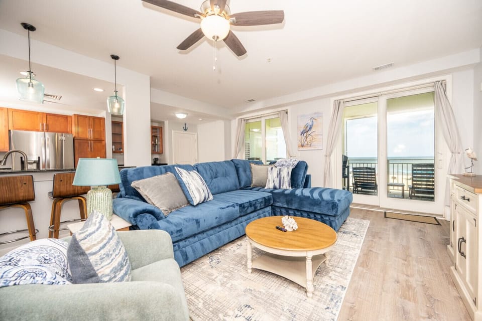 Spacious, light-filled living area with a plush sectional sofa, coastal décor, and seamless access to the balcony.