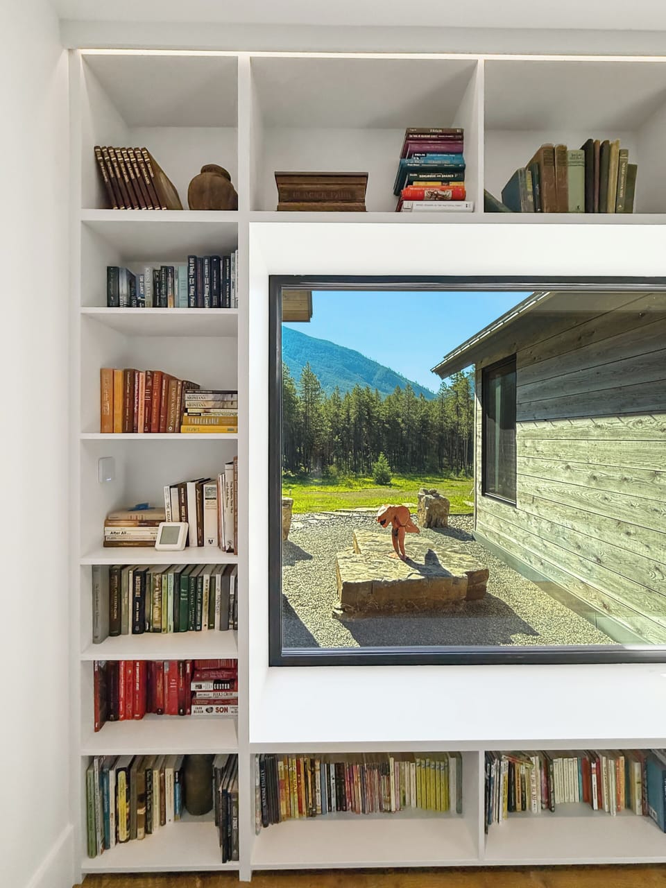 Cozy reading nook with built-in bookshelves, curated reads, and a picture window framing peaceful mountain views.