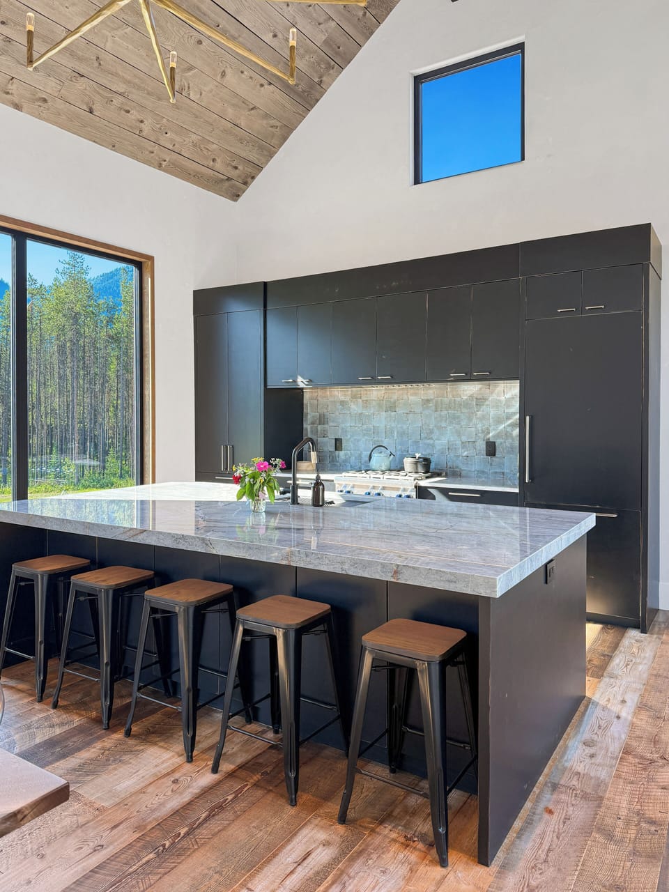 Sleek, well-equipped kitchen with a large stone island and forest views.