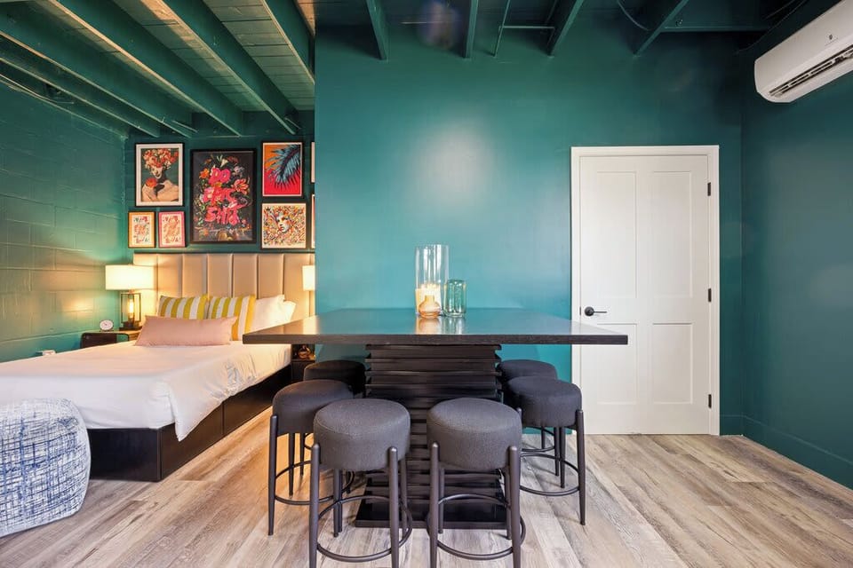This stunning space blends bedroom and living areas seamlessly! Teal walls, a comfy bed, vibrant art, and a chic sofa create an exciting, stylish, and highly functional retreat.