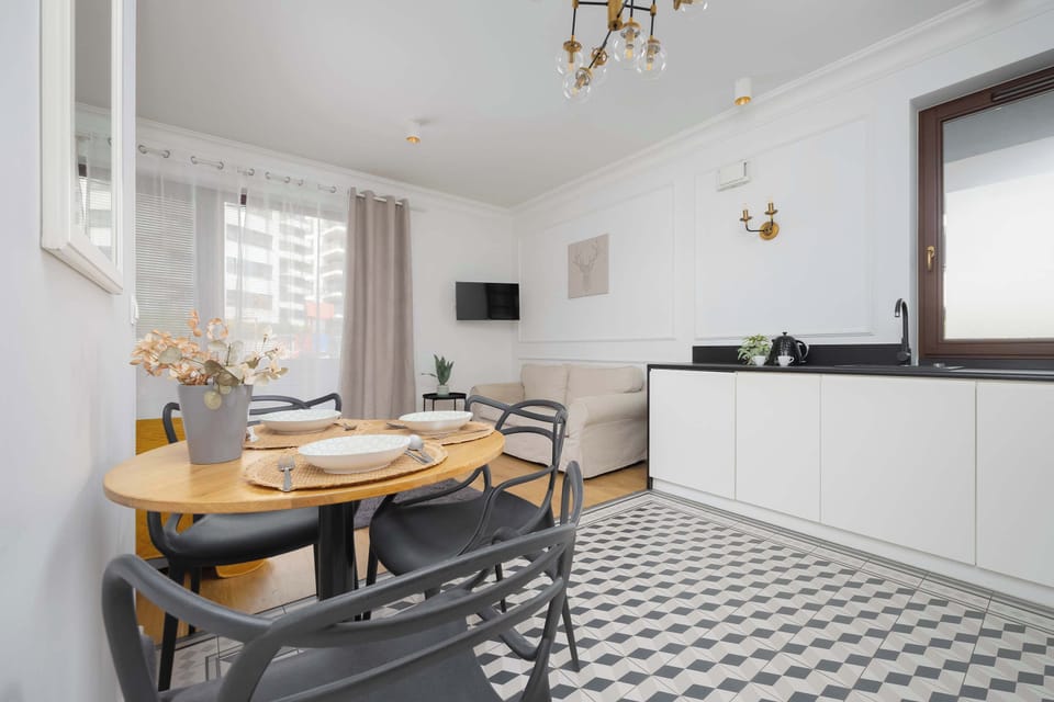 A full view of the main living space, showing the bed, dining table set for four, and kitchen area in a bright atmosphere.

