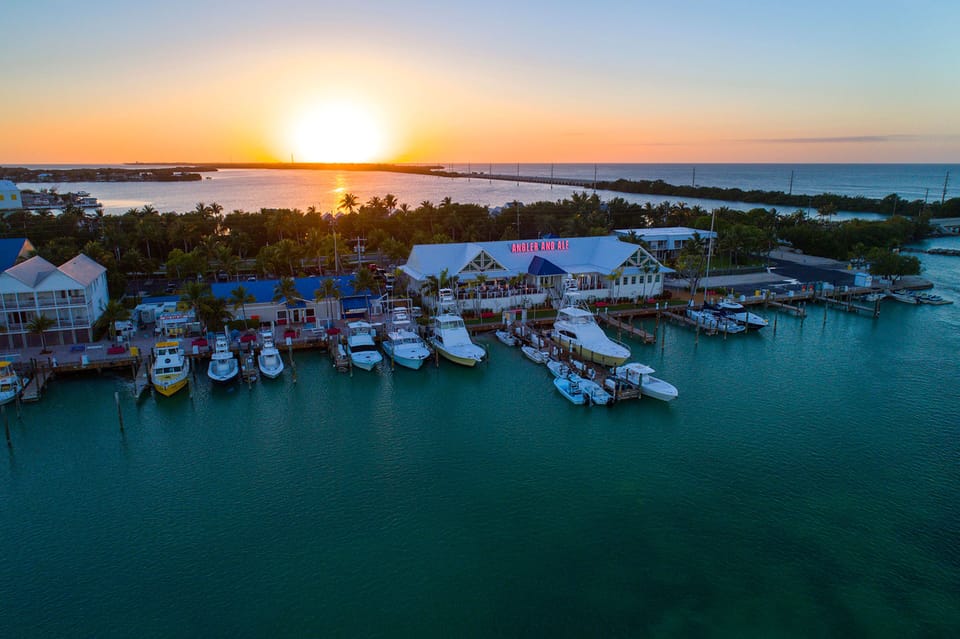 A breathtaking sunset casts golden light over the marina, where sleek boats rest on turquoise waters and the evening sky glows with tropical serenity.
