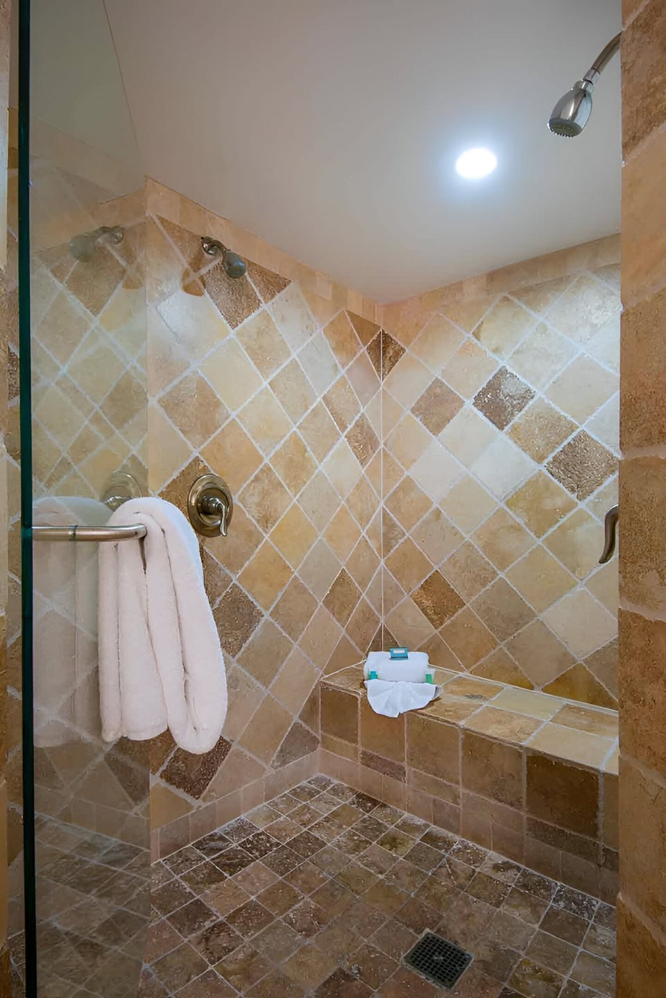 Ease into island time in a walk-in shower wrapped in warm stone and designed for restful pauses.