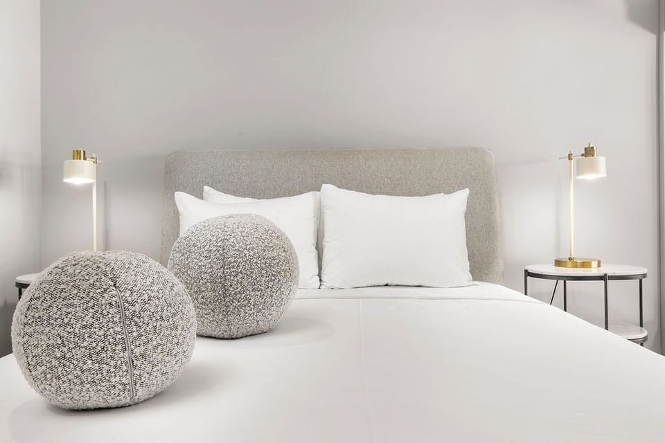 Bright and inviting bed setup with soft pillows, textured accents, and warm bedside lighting—perfect for unwinding after a day at the beach.