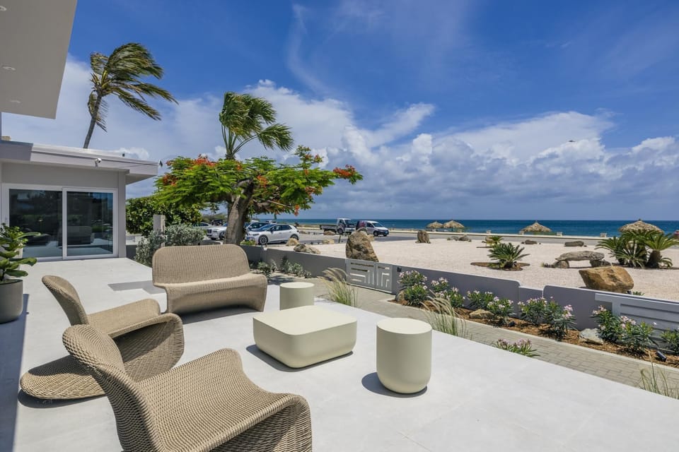 Spacious patio with modern seating, tropical landscaping, and panoramic views of the beach—your front-row seat to sea breezes, sunsets, and barefoot mornings.