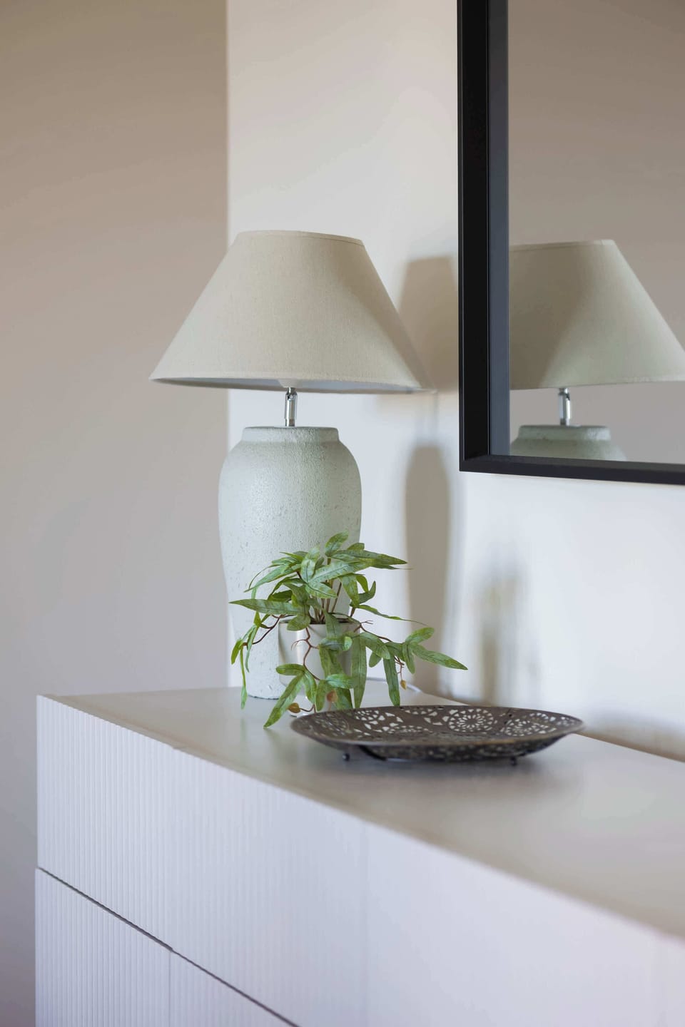 A white nightstand with a lamp and plant in a minimalist style.