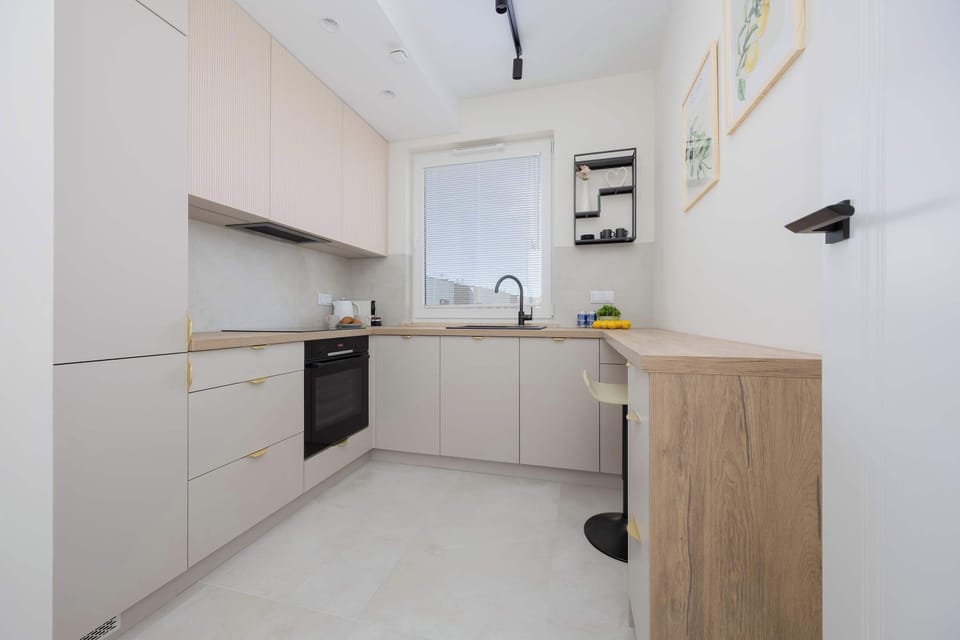 A kitchen corner with upper and lower cabinets, light tile flooring, and natural daylight.