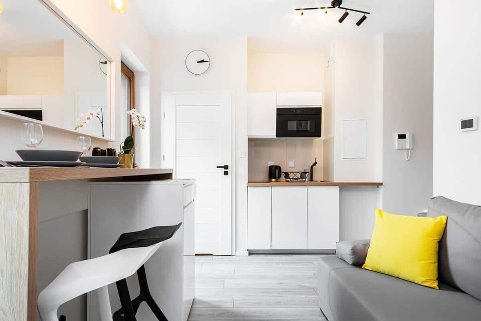A small, modern kitchen with white cabinetry, a microwave, and a dining area, providing everything needed for meal preparation in a minimalistic design.
