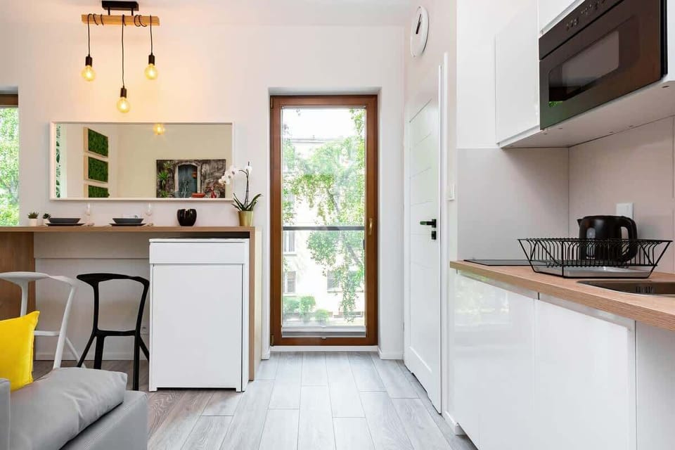 A clean and minimalistic kitchen area with white cabinetry and a large window, providing ample natural light and a pleasant cooking environment.