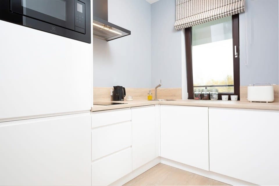 A clean and bright kitchenette featuring white cabinets and a window.