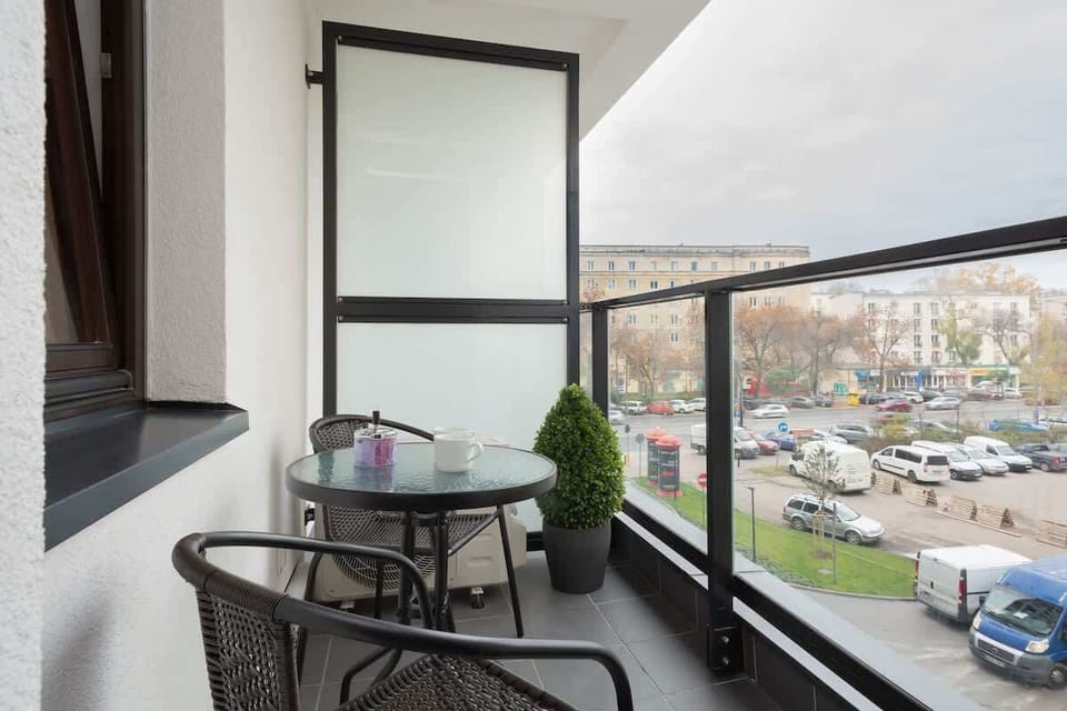 A small balcony with chairs and a table, overlooking a cityscape.