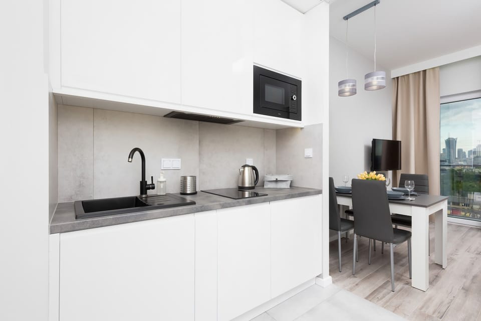 Functional kitchenette with white cabinets. There is an electric kettle on the grey countertop.
