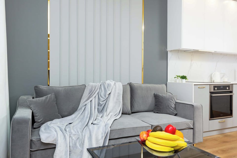 A stylish living room featuring a grey sofa and light-colored walls. A cozy throw blanket is draped over the sofa, with a bowl of fruit on the coffee table adding a touch of color.