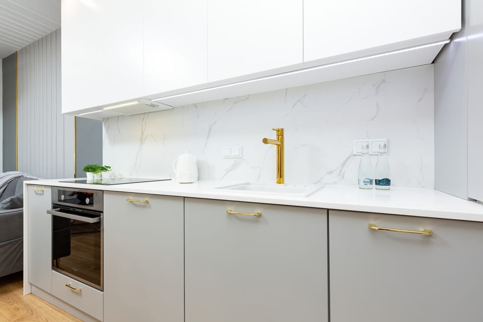 Modern kitchenette with white cabinets and gold faucet fixtures. The space includes built-in appliances like an oven and washing machine for convenience.