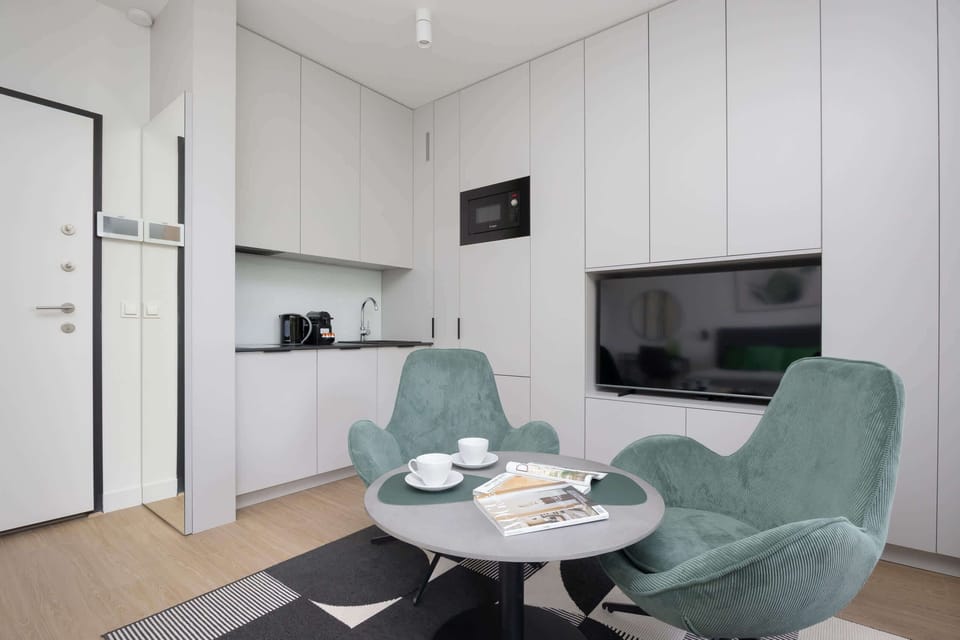 A cozy sitting area with two green armchairs, a round table, and a TV mounted on the wall.